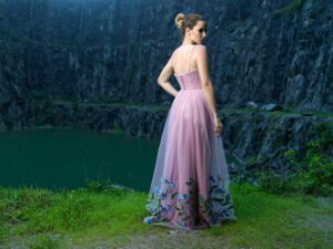 trendy clothes in 2026 A woman in a pink floral dress stands by a scenic cliffside outdoors, conveying elegance.