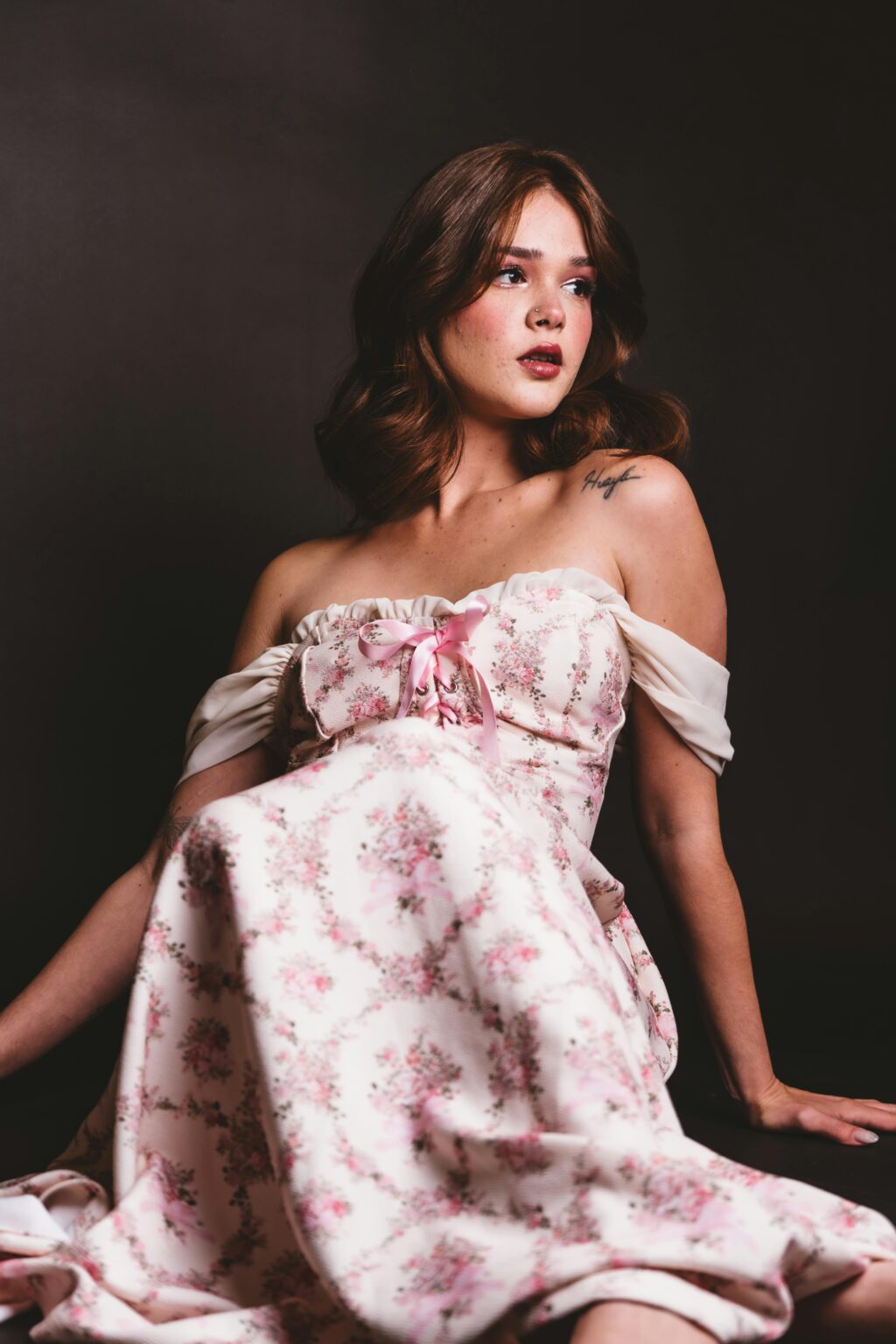 Portrait of a woman in an elegant floral dress, seated gracefully against a dark backdrop.