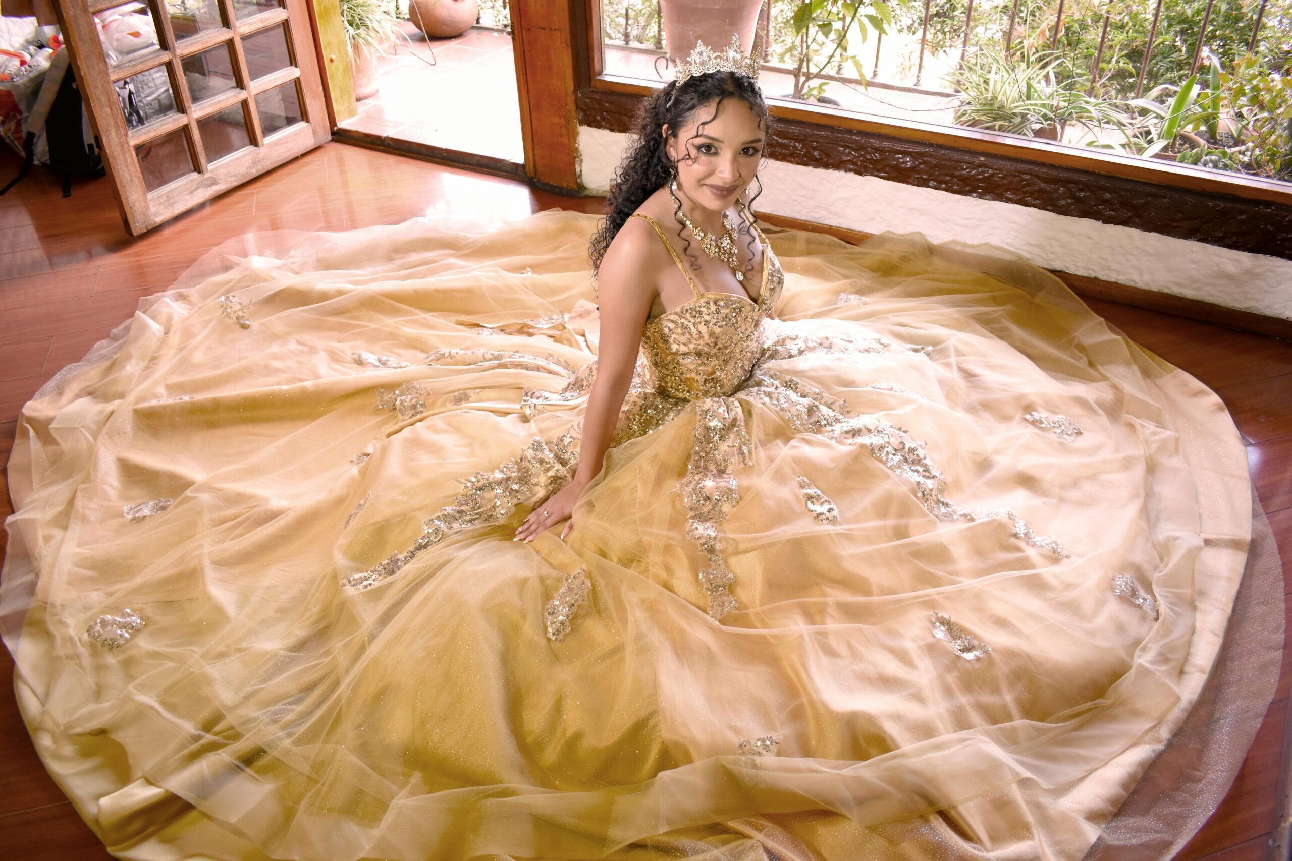 Young woman in stunning golden dress indoors, perfect for quinceañera celebrations.